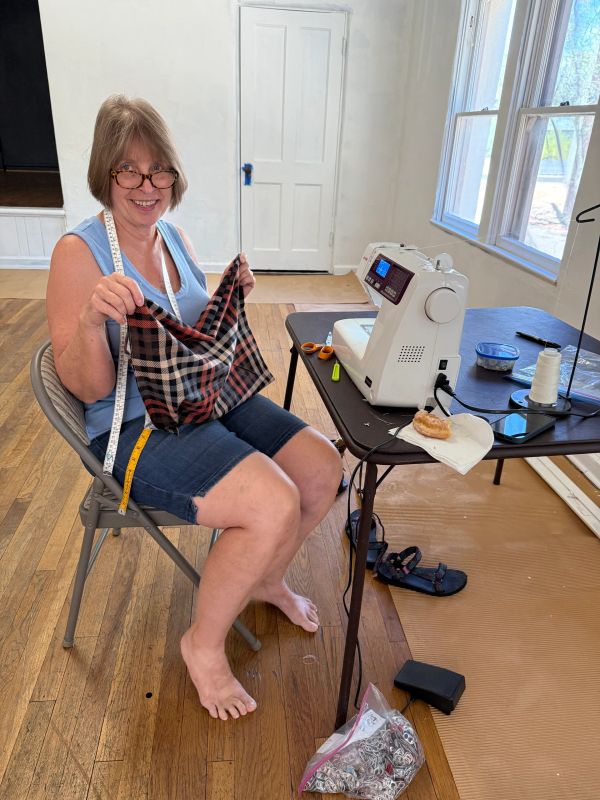 Smiling woman sewing with a sewing machine and fabric in a bright room.