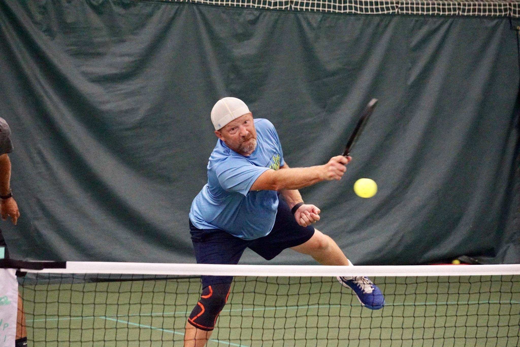 Action shot of a man hitting a pickleball over a net