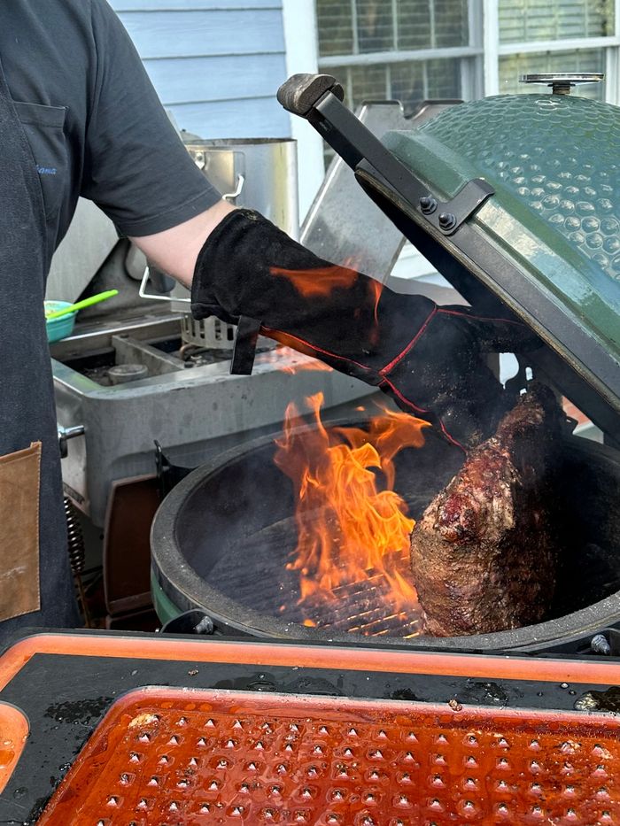 Man grilling meat over flames on a green ceramic grill outdoors.
