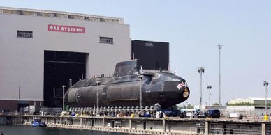 A submarine docked near a BAE Systems building.