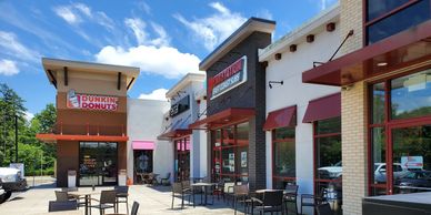 Outdoor seating area in front of a Dunkin' Donuts and other shops on a sunny day.