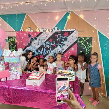 Children posing for a birthday photo with decorations and cake.