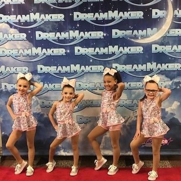 Four young girls in matching dance outfits pose on a red carpet at DreamMaker event.