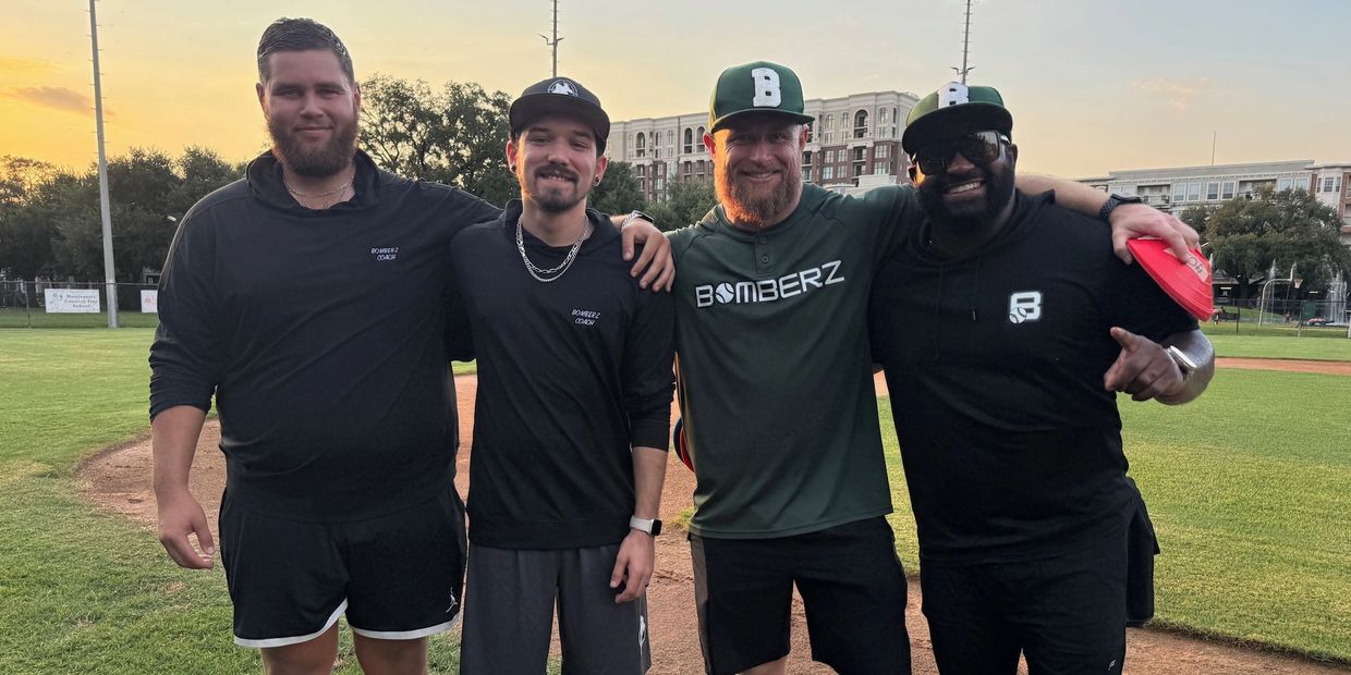 Four men posing on a baseball field at sunset, wearing Bomberz gear.