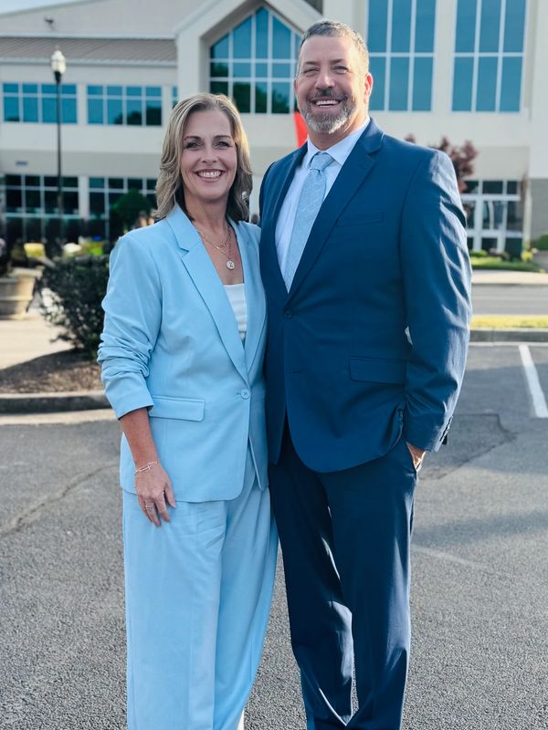 A smiling couple dressed in blue suits posing outdoors.