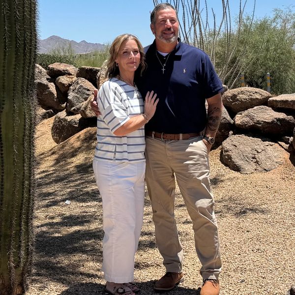 Couple posing outdoors in a desert landscape with rocks and cacti.