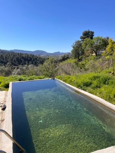 Outdoor pool with clear water overlooking green hills and blue sky.