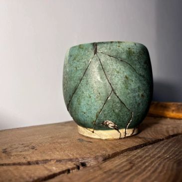 Petit vase en céramique fissuré posé sur une table en bois.