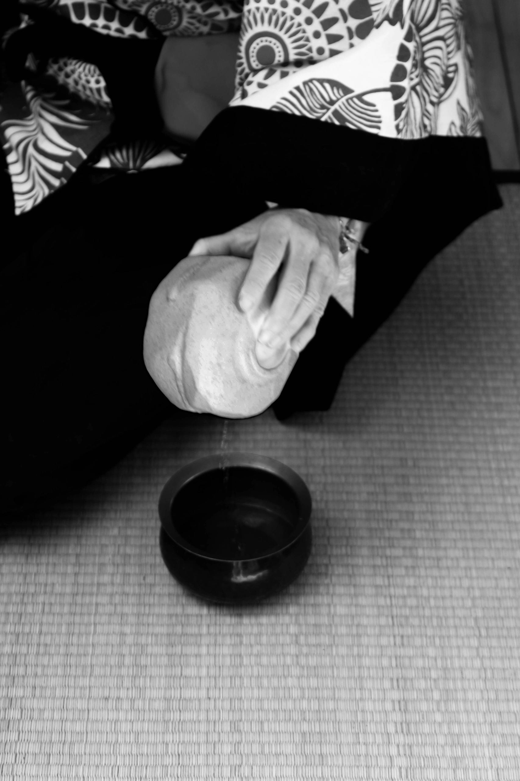 Person pouring tea from a cloth-covered pot into a bowl in a traditional setting.