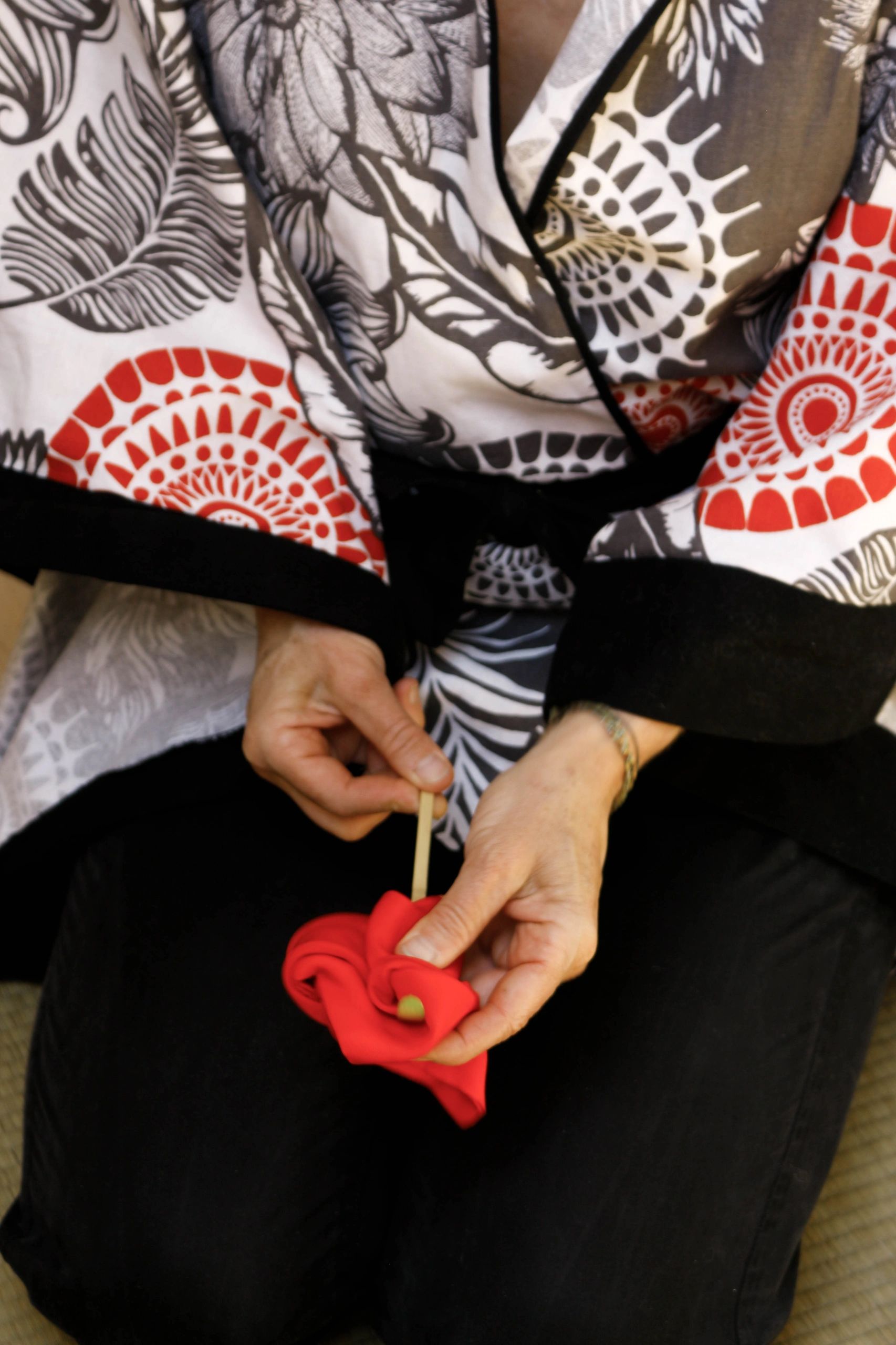 Hands holding a red flower, wearing a patterned kimono-style robe.
