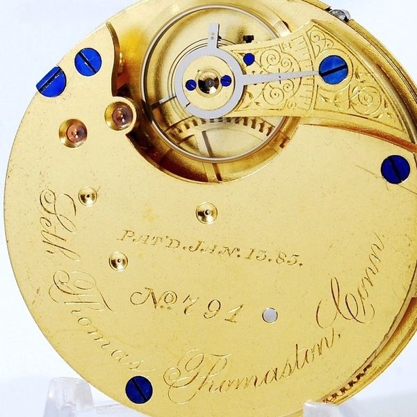 Antique gold watch movement with intricate engravings and blue screws.