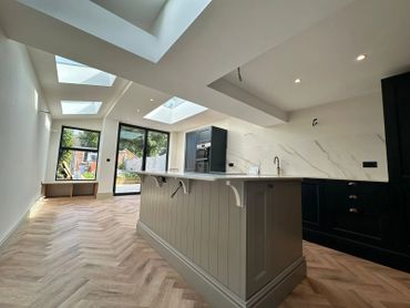 Modern kitchen with black cabinets, marble backsplash, and natural light from skylights and large windows.
