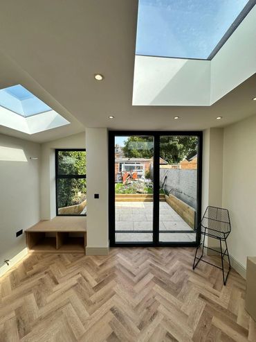 Bright modern room with skylights, herringbone floor, and glass doors to a patio.