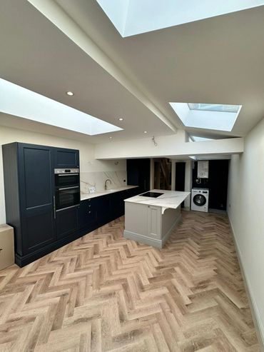 Modern kitchen with black cabinetry, gray island, and skylights illuminating a wood-patterned floor.