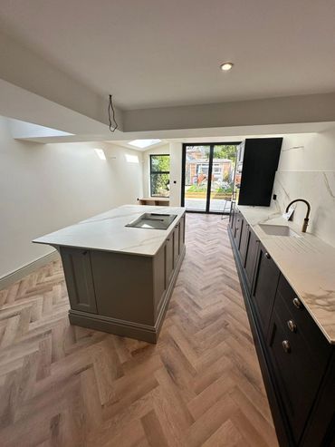 Modern kitchen with marble countertops and herringbone wood flooring.