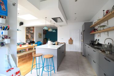 Modern kitchen with gray cabinets, blue stools, and open shelving.