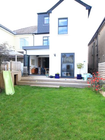 Backyard with green lawn, slide, and modern house with open doors.