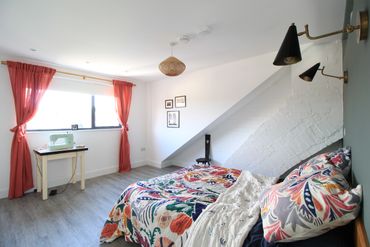 Bright bedroom with colorful bedding and coral curtains by a sewing machine.