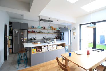 Modern kitchen with grey cabinets, island, and large windows brightening the space.
