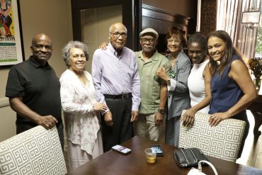 Group of six adults smiling around a dining table indoors.