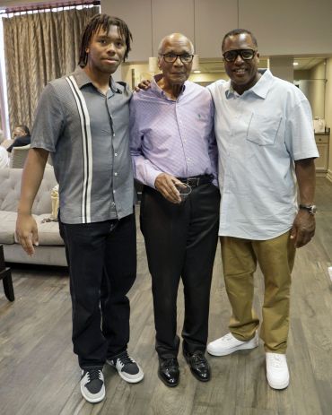 Three men standing together indoors, smiling.