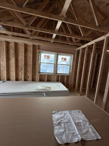 Interior of a house under construction with exposed wooden framing and windows.