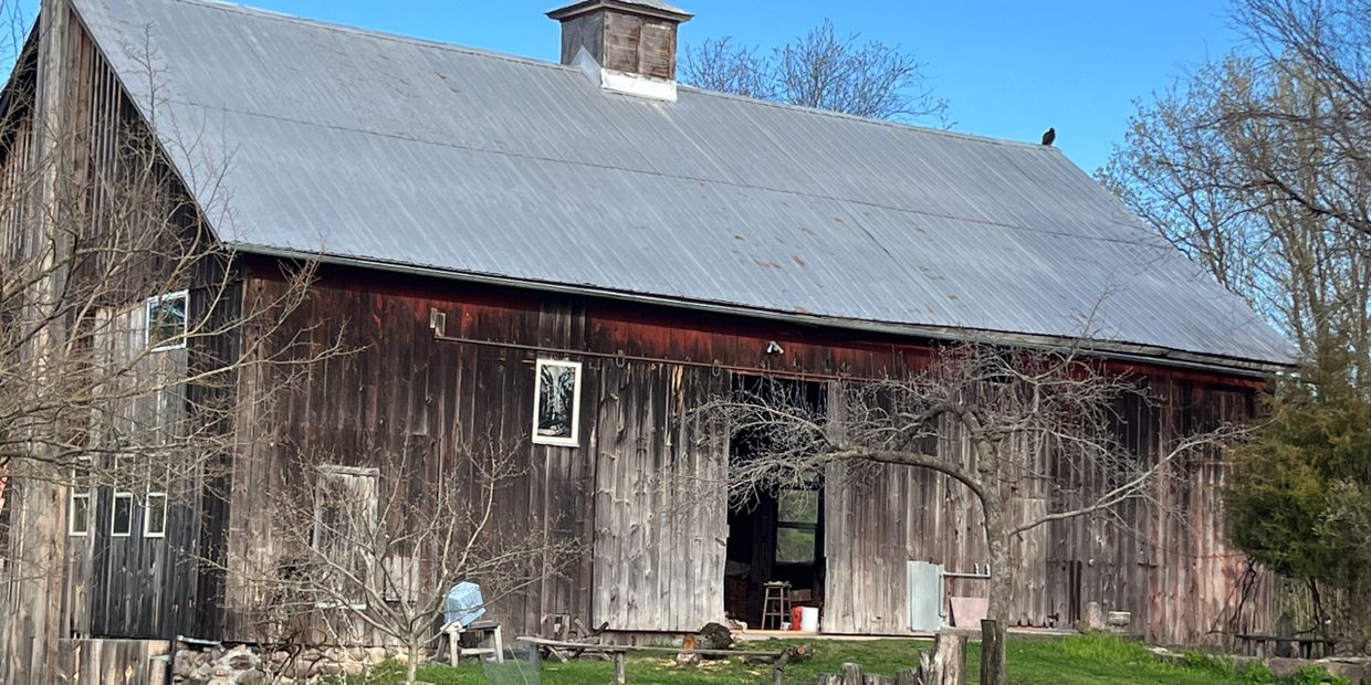 Old wooden barn with a metal roof under a clear blue sky.