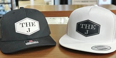 Two caps, one black and one white, both with 'THE J' logo.