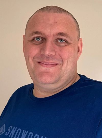 Smiling man with blue eyes and a shaved head wearing a navy blue shirt.