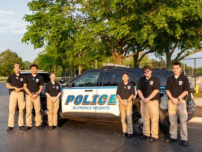 cadets standing, face forward, holding their hands in front of the Glendale Heights Police vehicle