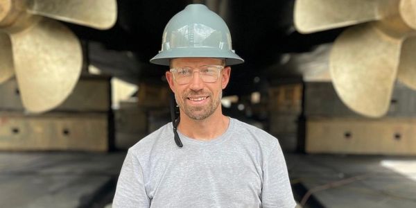Man in safety helmet standing between two large ship propellers.