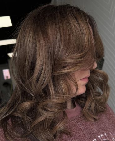 Soft brown hair styled in loose curls with side-swept bangs.