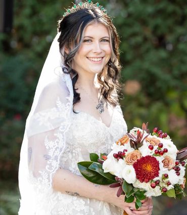 Smiling bride in white lace dress holding a vibrant bouquet outdoors.