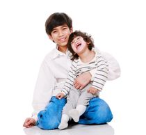 A boy holding his physically challenged little brother. Both are smiling. 