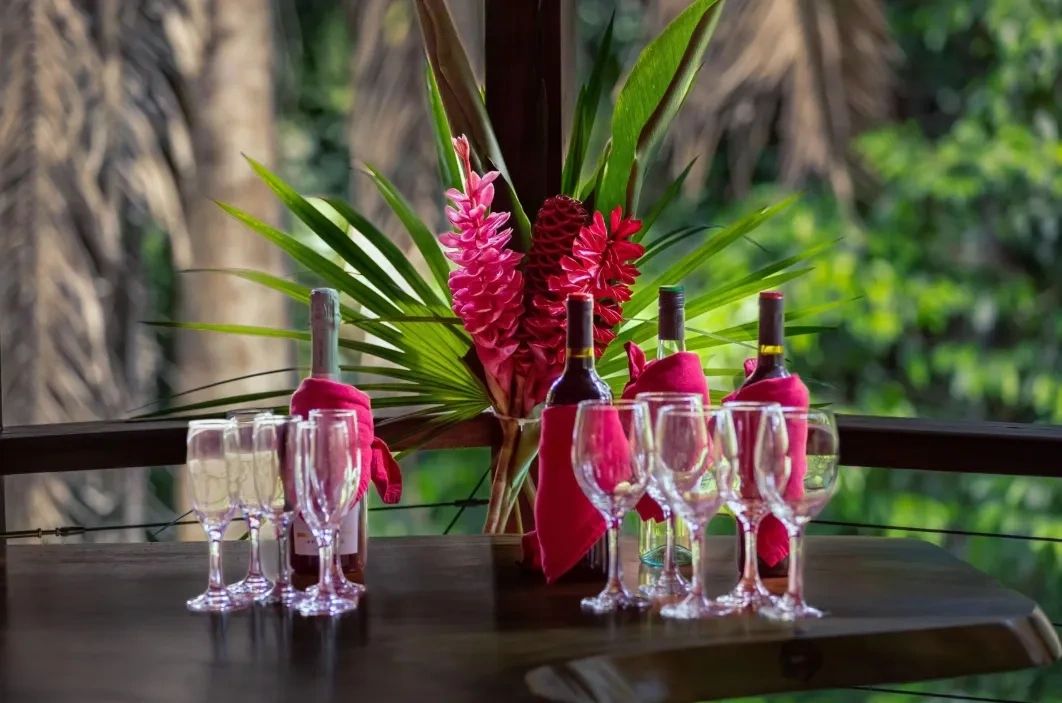 Wine bottles and glasses on a table with tropical flowers.