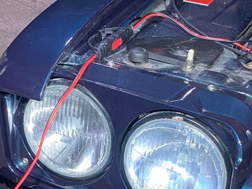 Close-up of a car's dual round headlights and exposed wiring under the hood.