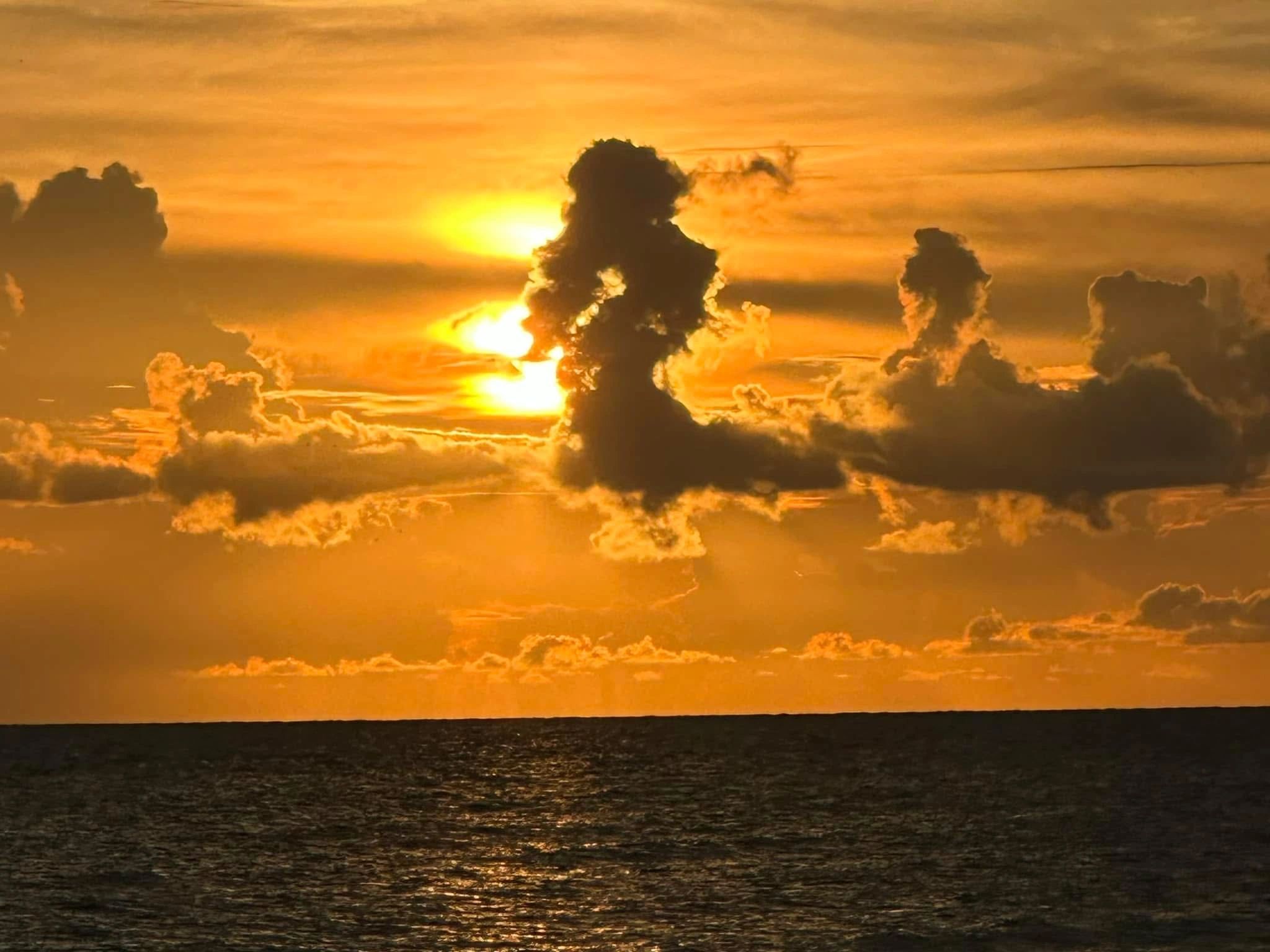 Sunset over ocean with dramatic clouds glowing orange.