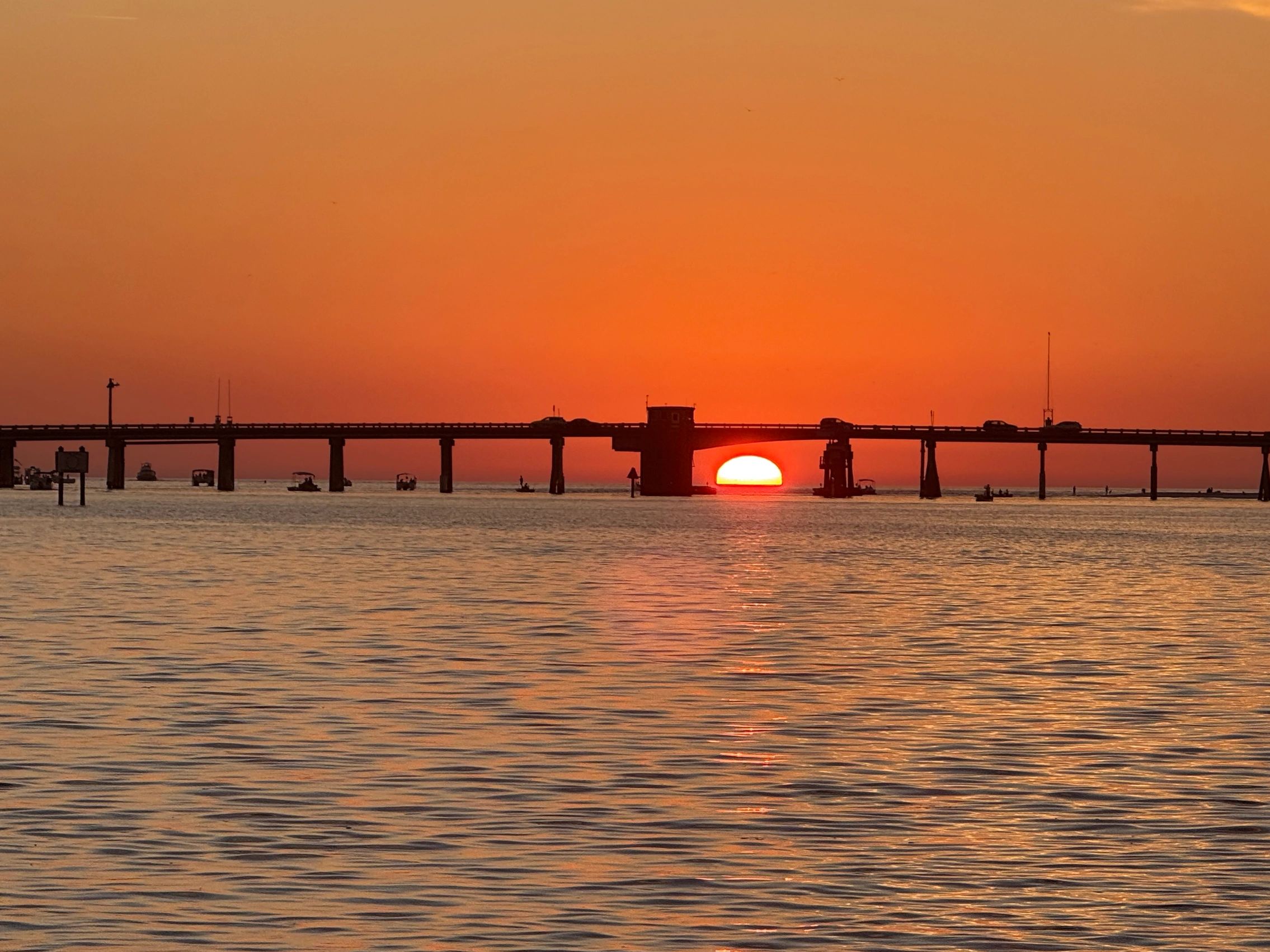 Sunset behind a bridge over calm water with boats.
