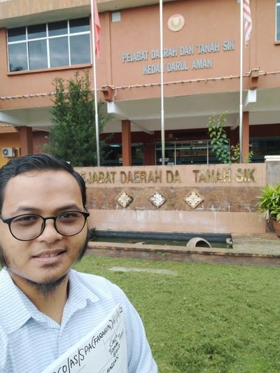 A man taking a selfie in front of the Sik District Office building in Kedah, Malaysia.