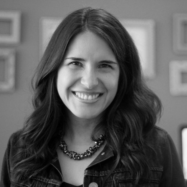 A smiling woman with long hair wearing a necklace and denim jacket.