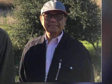 Man wearing glasses, a cap, and a dark jacket outdoors.
