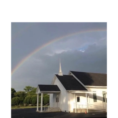 White church building under a rainbow in a cloudy sky.
