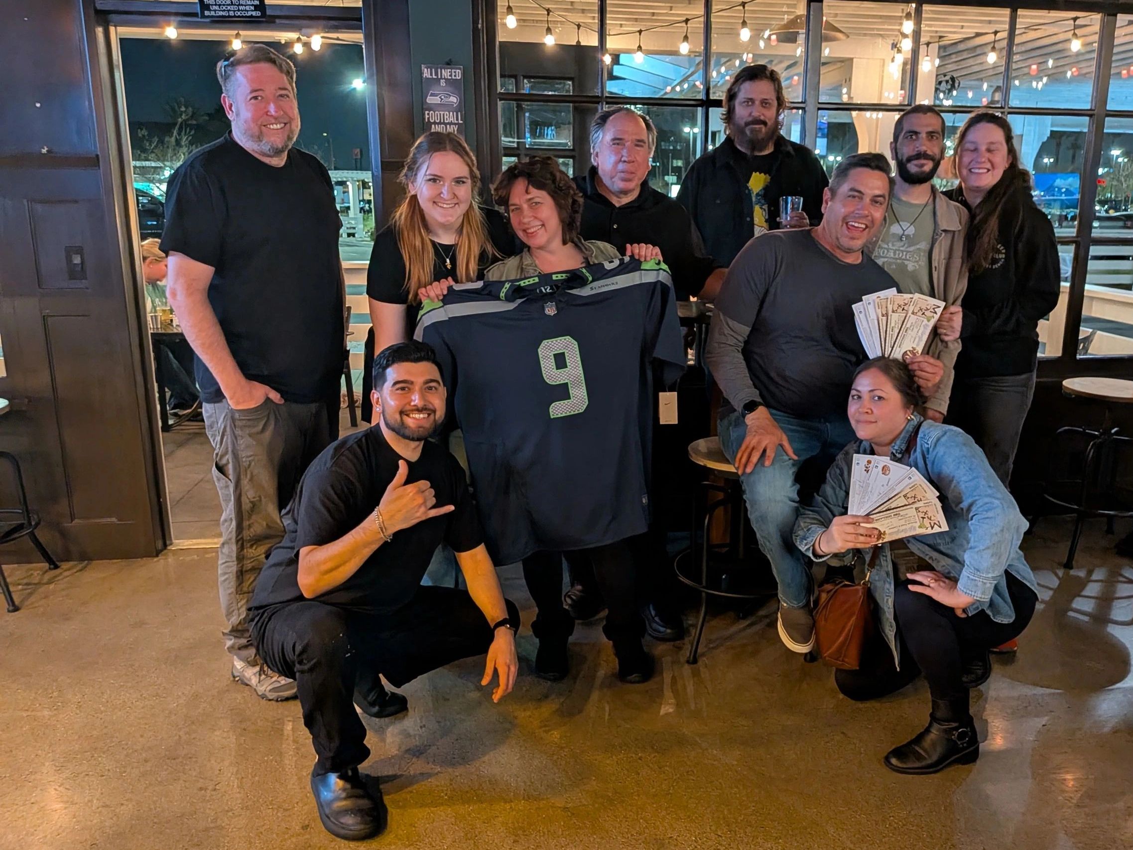 A cheerful group holding a Seahawks jersey and tickets indoors.