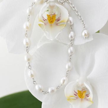 Pearl necklace draped over white orchid flowers.