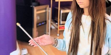 A woman holding a selfie stick indoors with long hair and casual clothes.