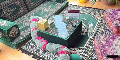 Cozy living room with patterned carpets and a large knitted snake on the floor.