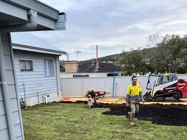 Workers installing new grass in a backyard with one man walking and a toddler with an adult in the background.