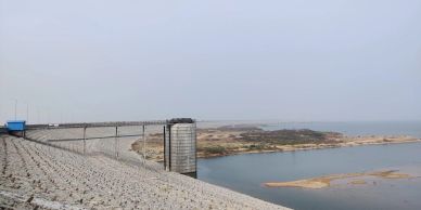 A dam with water reservoir and rocky embankment under a cloudy sky.