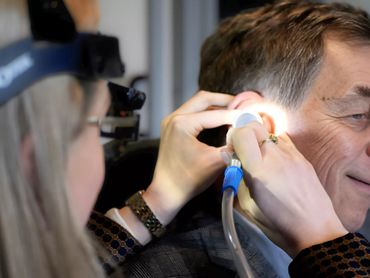 A doctor examines a man ear with a medical instrument.