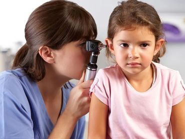 A nurse examining a young girl ear with an otoscope.
